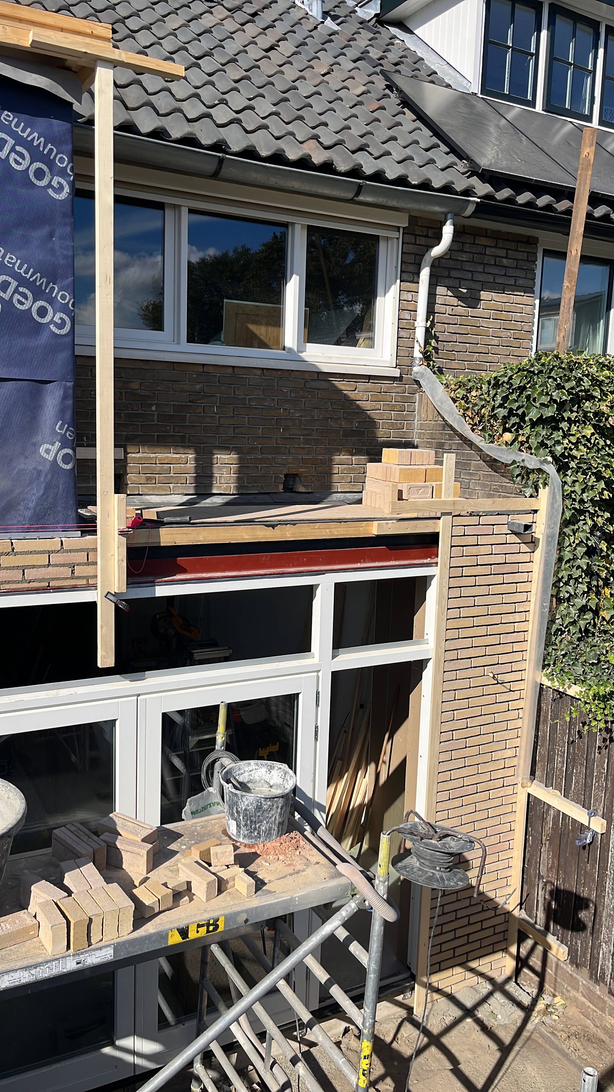 Nieuw metselwerk rondom de kozijnen van de uitbouw, met een stapel stenen op de steiger