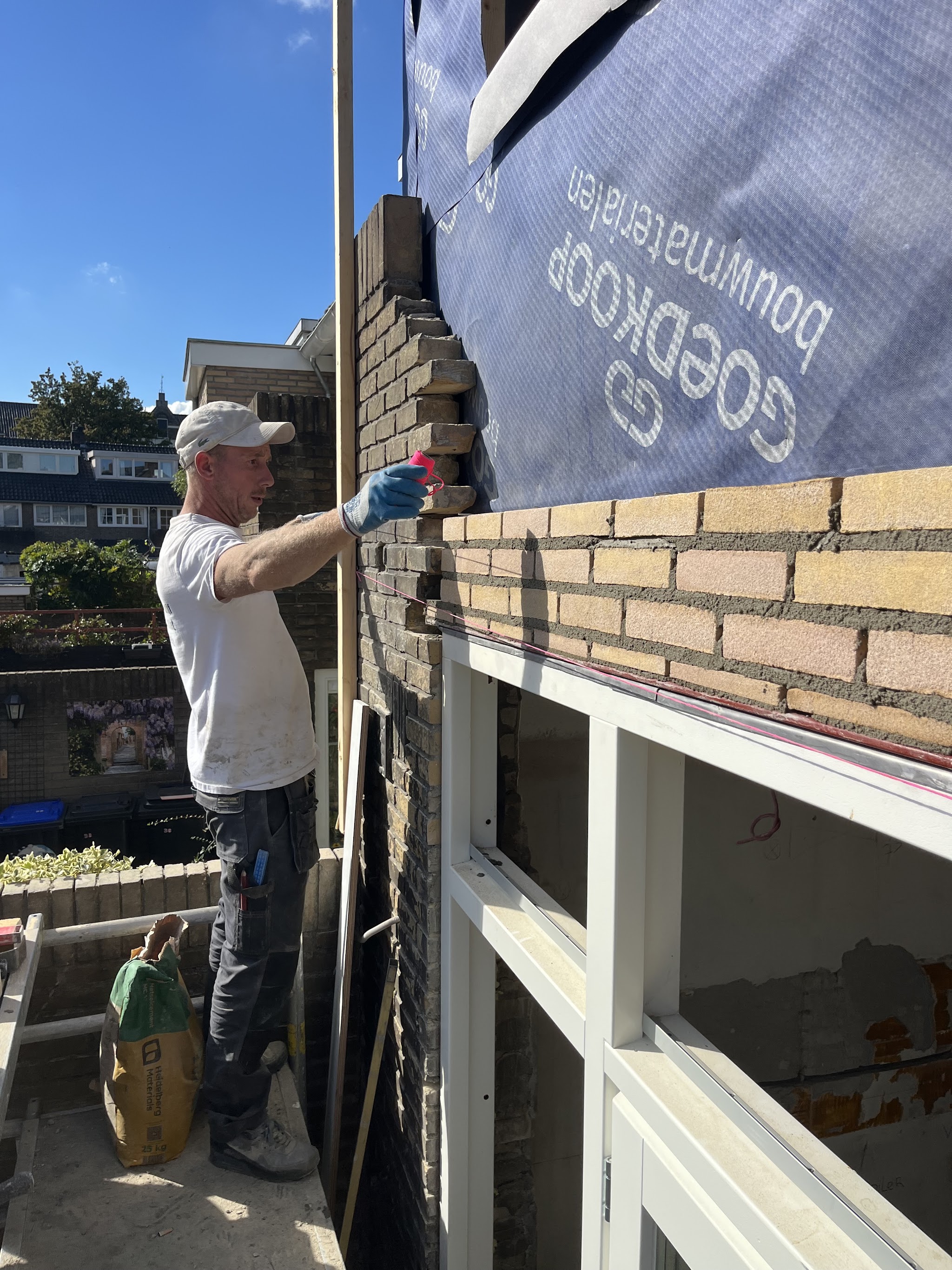 Michael van Vliet metselt een gevel op de steiger, met een blauwe hemel erboven