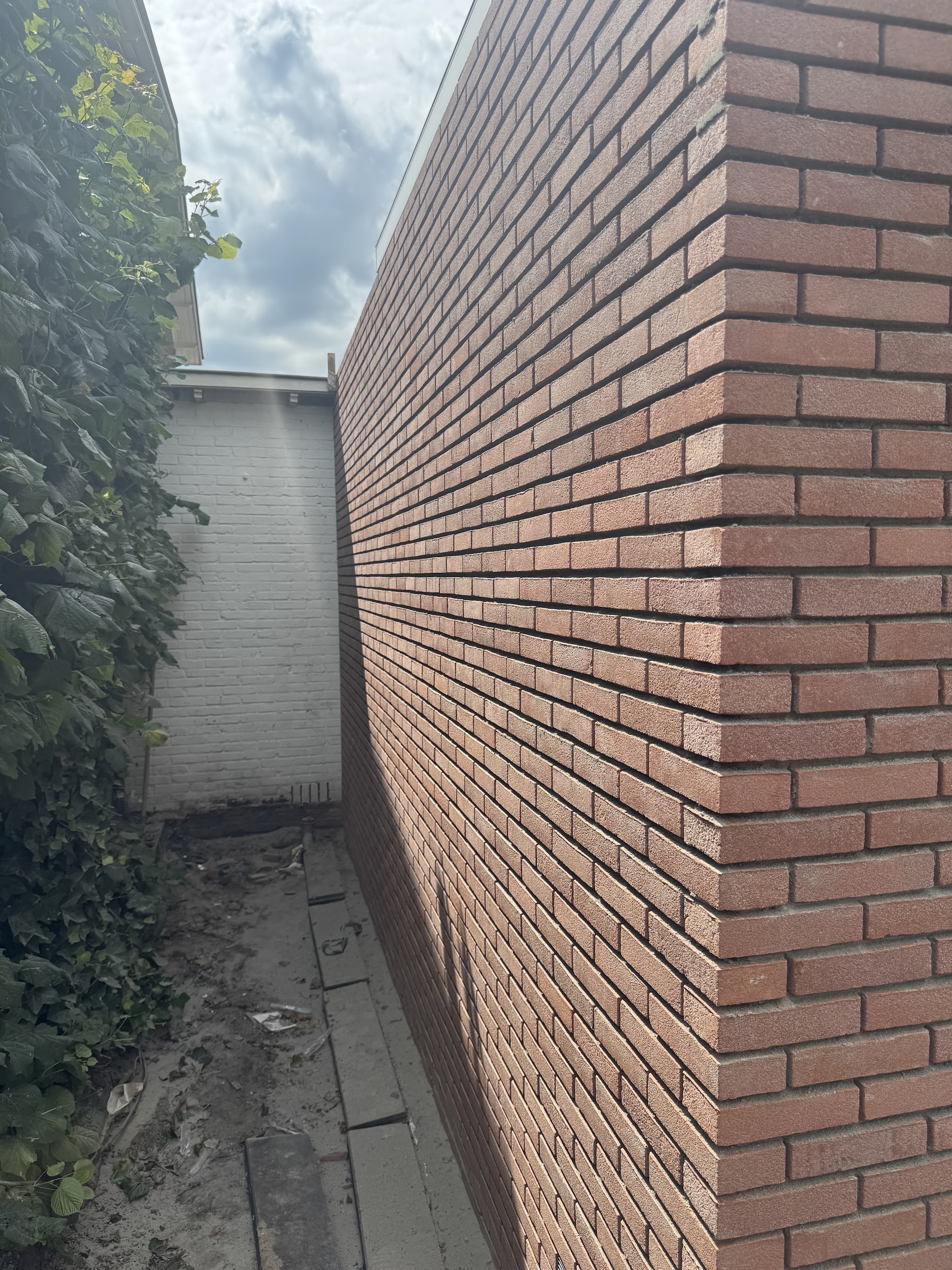 Nieuwe rode bakstenen tuinmuur langs een tuinpad, met een strakke hoek en schone voegen