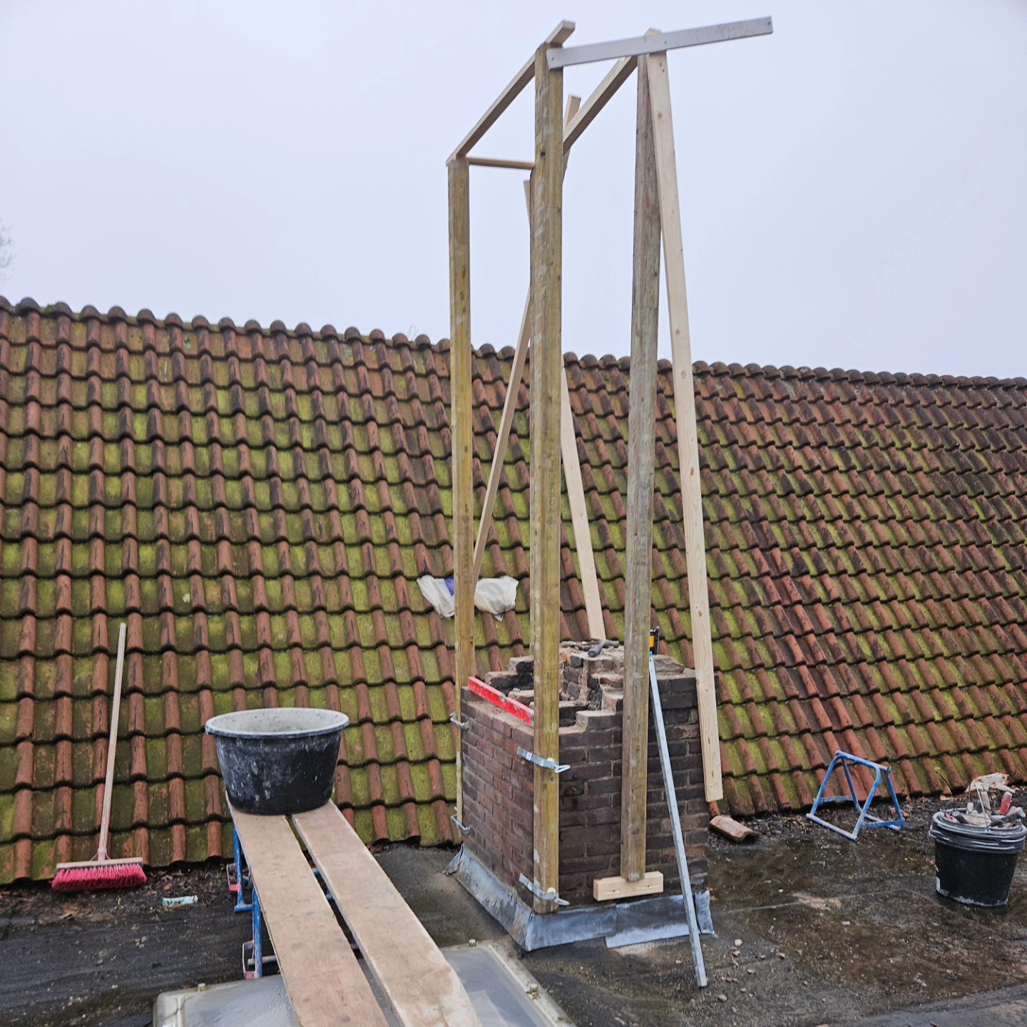 Schoorsteen die opnieuw wordt opgemetseld binnen een houten steiger op een pannendak